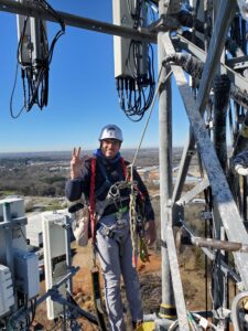 Guy making a piece sign while standing on a cell tower surrounded by antennas